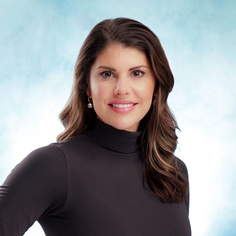 Smiling woman in black turtleneck, blue background.