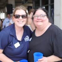 Two women smiling, holding blue cups.