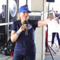 Woman speaking with microphone, pointing outward.