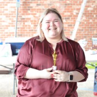 Smiling person holding a small gold trophy.