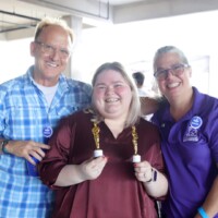 Three people smiling with small trophies.