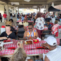 Outdoor gathering with people eating at tables.
