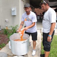 Two men cooking outdoors with large pot.