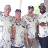 Four men in matching tropical shirts smiling.