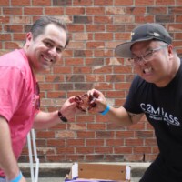 Two men holding a crawfish, smiling outdoors.
