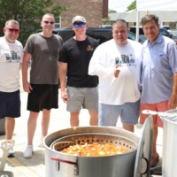 Five men standing near large cooking pots.