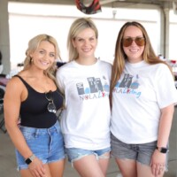 Three women smiling at outdoor event.