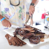 Man slicing grilled meat on cutting board.