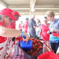 People serving and eating crawfish at event.