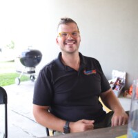 Smiling man sitting outdoors near grill.