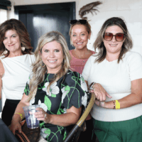 Four women smiling at an indoor gathering.